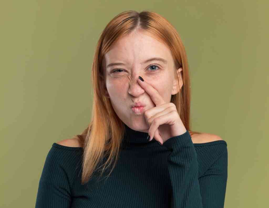 annoyed young redhead ginger girl with freckles puts finger nose looks camera olive green