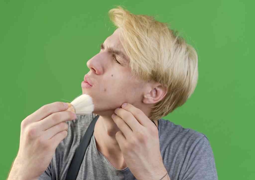 professional barber man apron holding shaving brush touching his face with it looking displeased